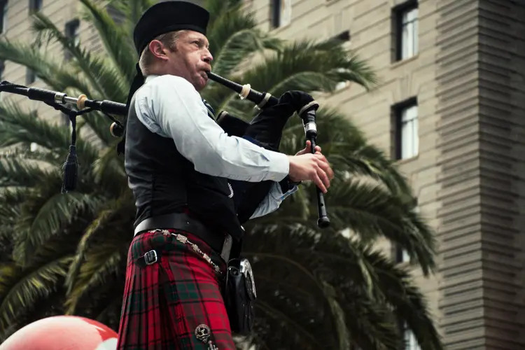 A kilted bagpiper in traditional Scottish attire, playing the bagpipes.