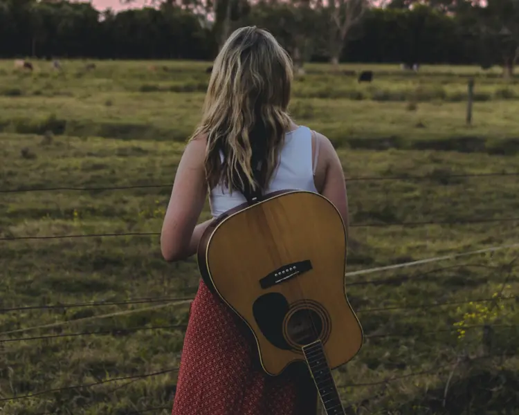 A girl out in nature with a guitar on her back.