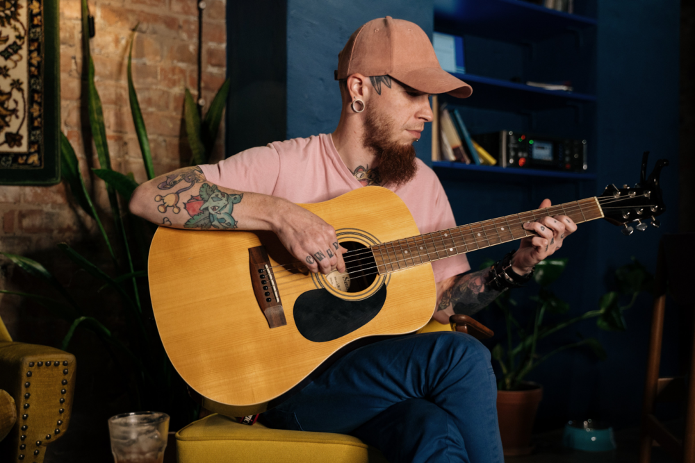 A young man with a tattoo playing an acoustic guitar