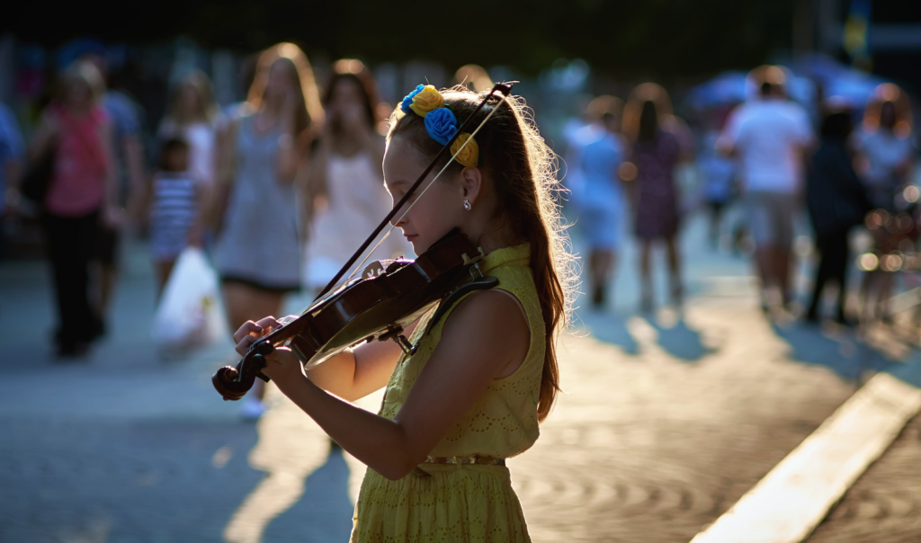 A young girl playing the violin in a street full of people