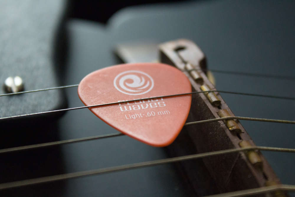 A triangle pick slotted underneath the strings on a fretboard.