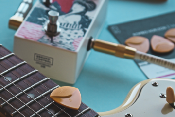 A close up of a guitar neck, guitar pedal, and a guitar pick.