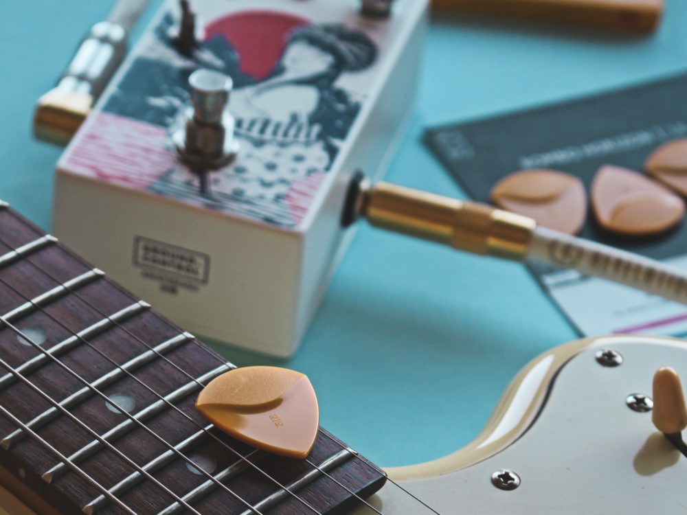 A close up of a guitar neck, guitar pedal, and a guitar pick.