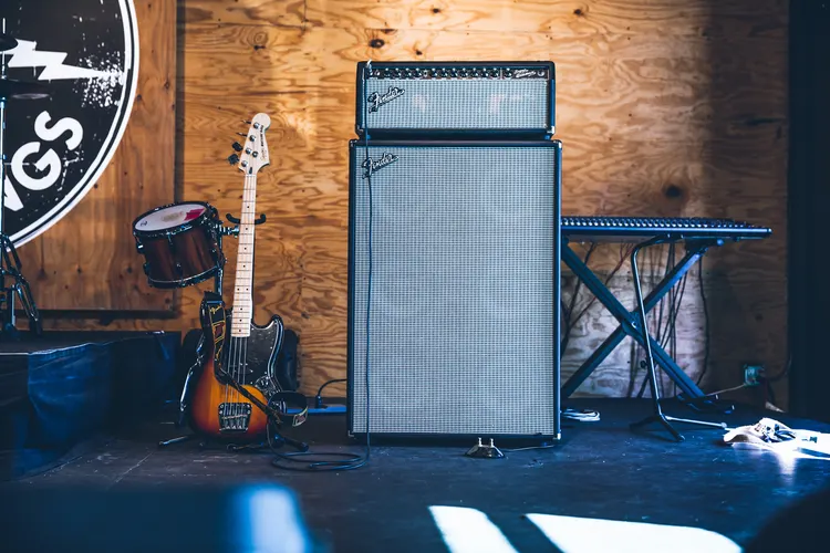A Fender amp on a stage with a guitar and keyboard.