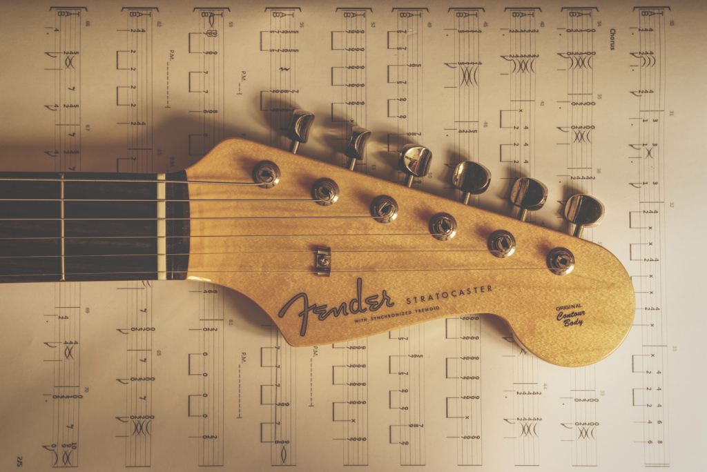 The headstock of a Fender Guitar lying on top of some sheet music.