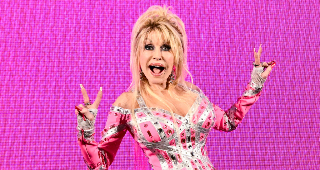 Dolly Parton posing against a bright pink background.