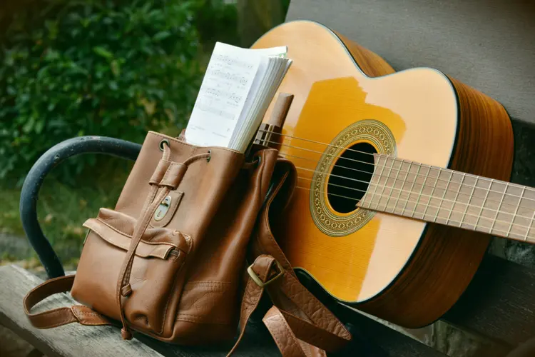An acoustic guitar with a leather bag leaning against it.