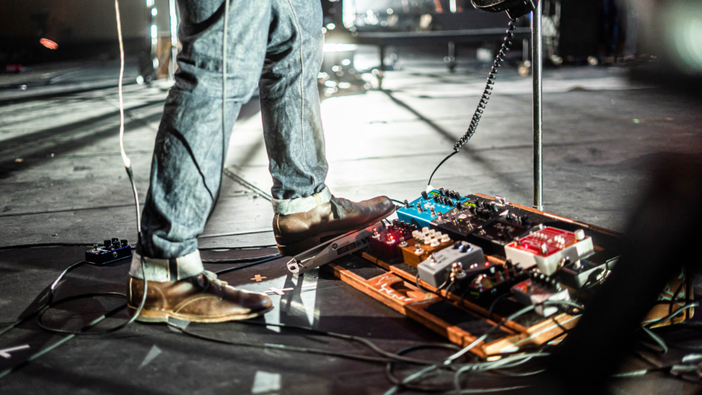 A close up of a musician using various guitar pedals.