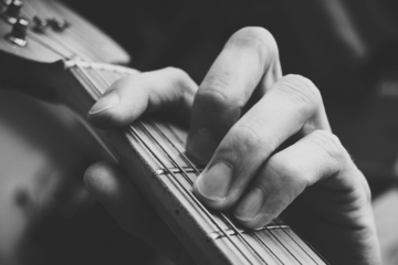 A black an white image of a person playing an f chord on the guitar fretboard.