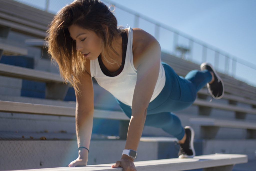 A woman in workout clothes doing planks at a stadium.