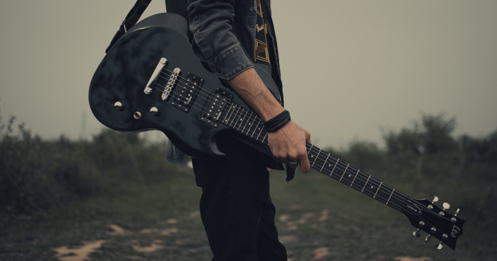 A holding an electric guitar on the side of the road.