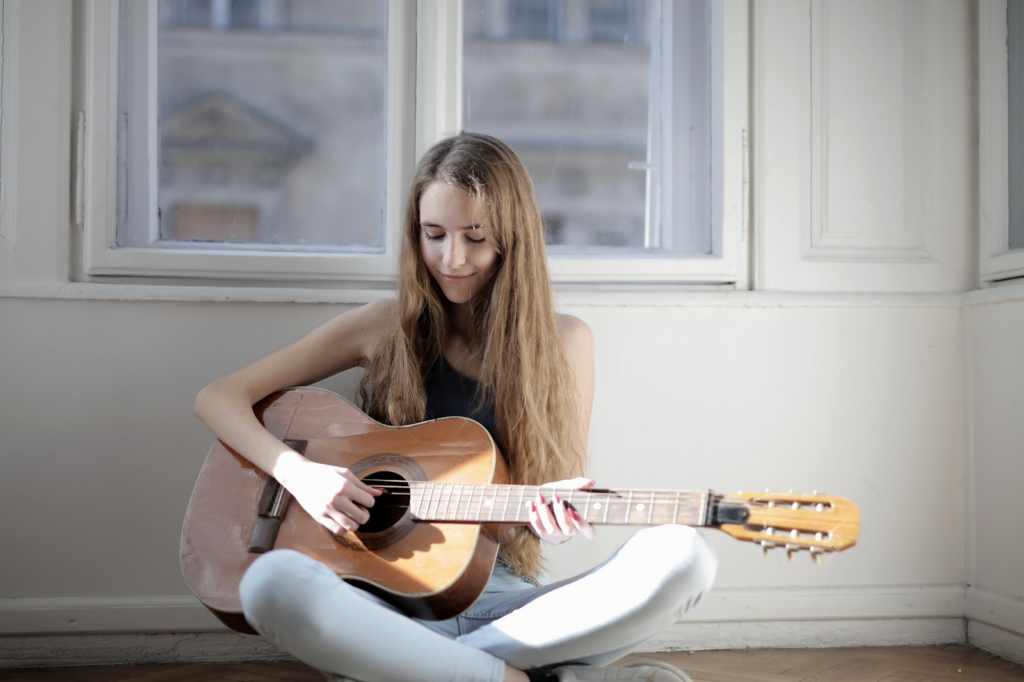 A woman sitting on the floor while playing guitar.