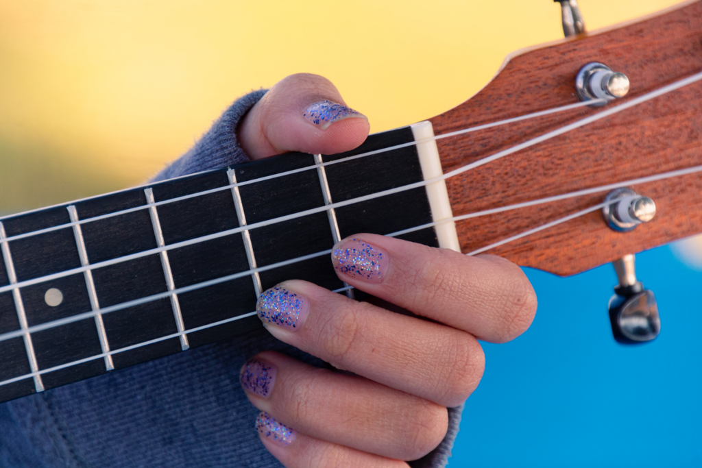 A close up of a woman's fingers with glitter nail polish on the fretboard of a guitar.