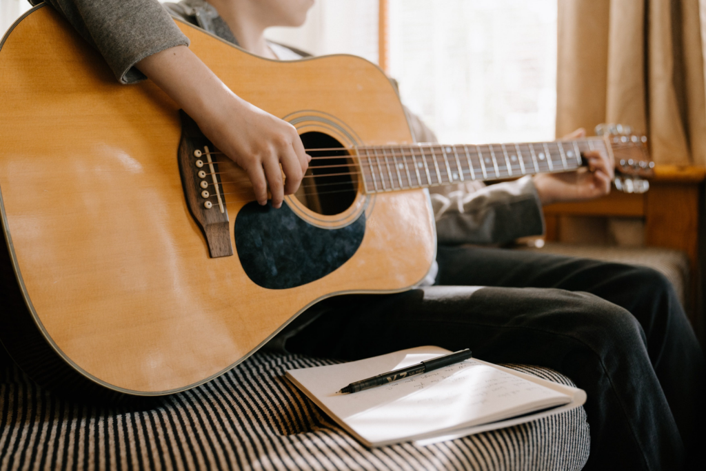 A person playing guitar with a notebook and a pen.