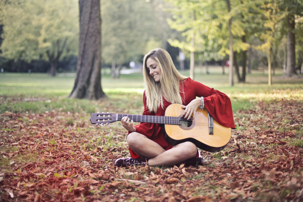 A woman in a red dress playing the guitar in a forest.