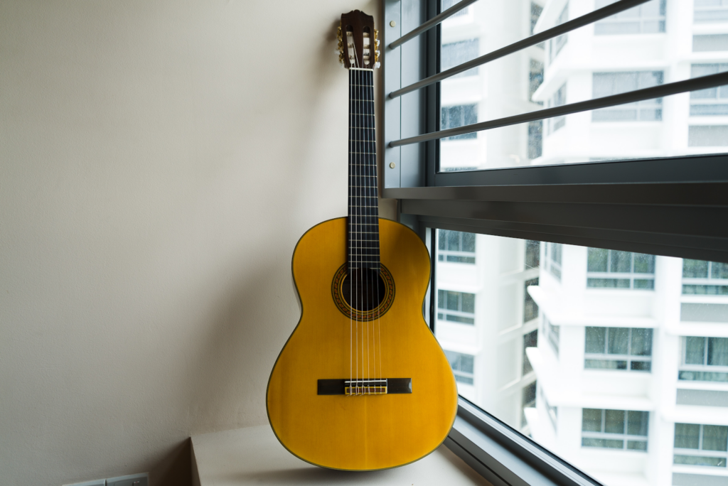 An acoustic guitar placed upright next to a window.