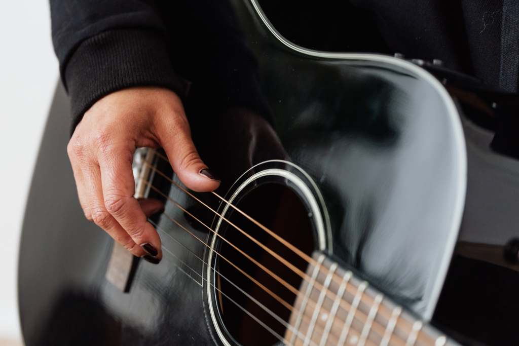 A black acoustic guitar being played by someone with black nail polish.