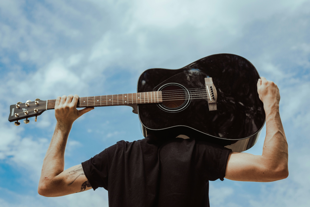A man with an acoustic guitar on his shoulders, looking up at the sky.