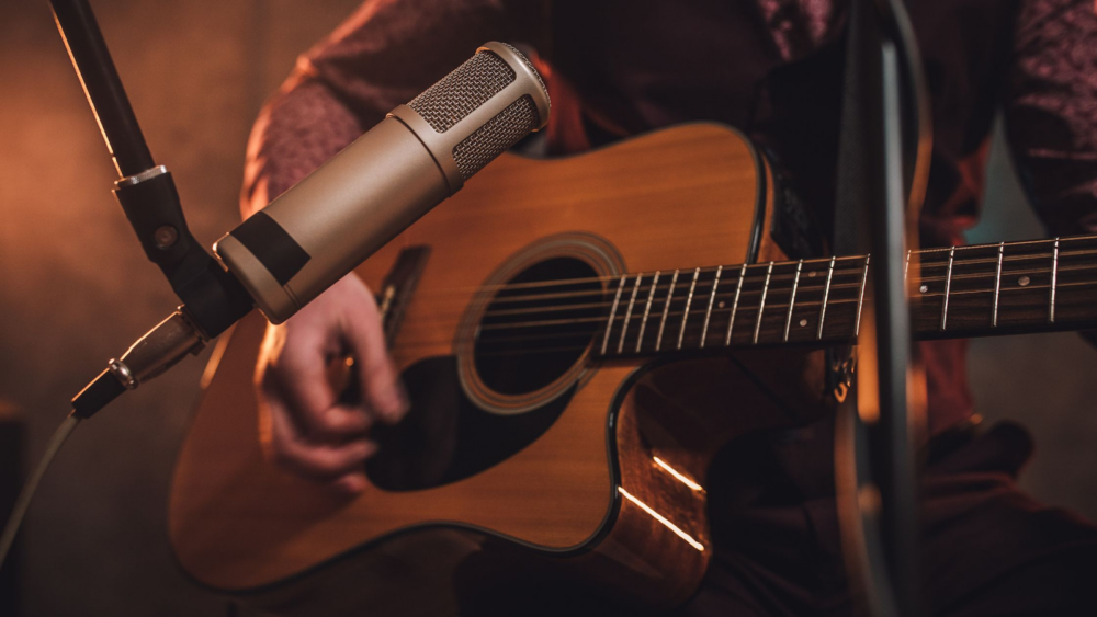 An acoustic guitar being strummed in front of a recording microphone.