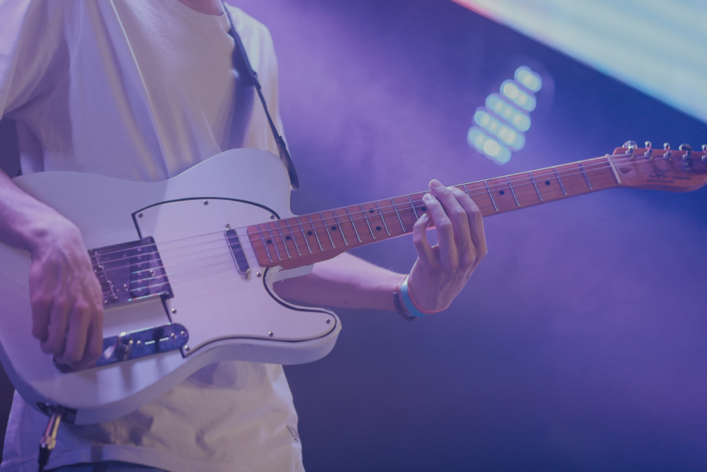 A man playing a white electric guitar on stage.