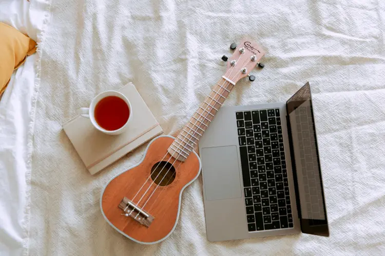 A ukelele next to a laptop and a cup of tea.
