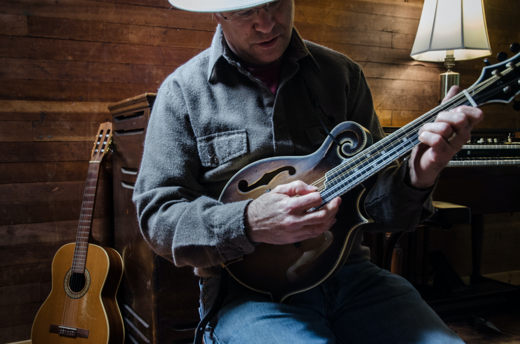 A man wearing a cowboy hat, playing a mandolin.