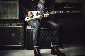 A guitarist surrounding by different amps, while he plays guitar.