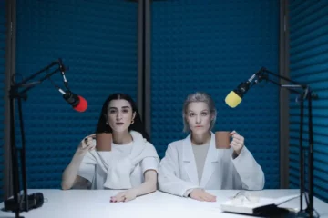 Two women in a recording booth lined with soundproof panels.