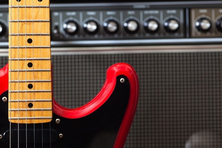 A red electric guitar standing against an amp.