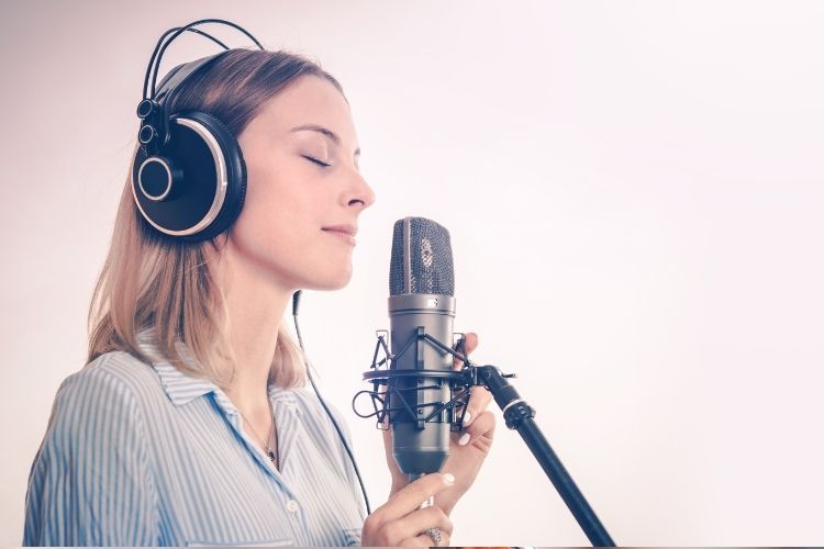 A women standing behind a recording mic, with a set of headphones on.