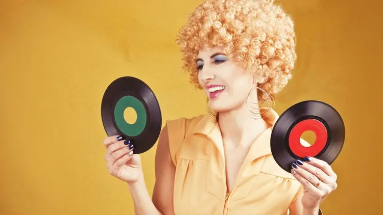 A lady dressed in clothes from the 70s holding vinyl records.