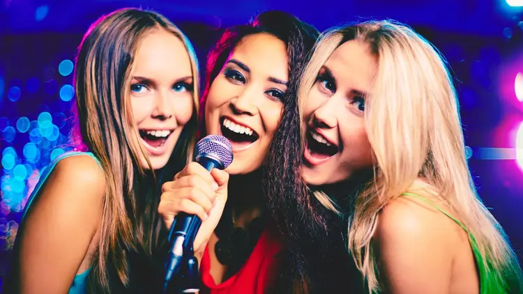 Three women sharing a mic, singing karaoke.